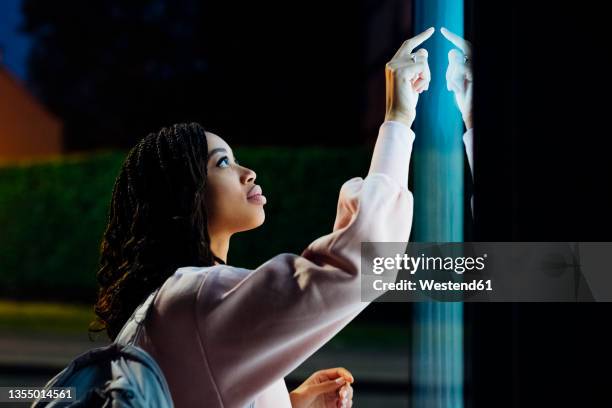 young woman touching kiosk screen at night - booth stock pictures, royalty-free photos & images