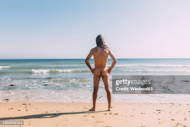 naked man with hand on hip at beach - beach bum foto e immagini stock