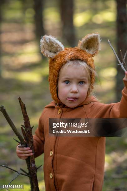 cute girl with wooden sticks sticking out tongue in forest - tierohr stock-fotos und bilder