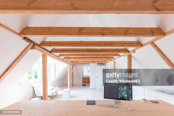 home attic with computer monitor on wooden table in foreground - holzbalken stock-fotos und bilder