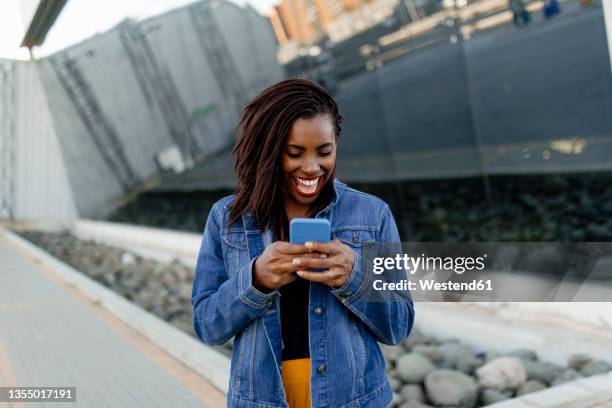 happy woman in denim jacket using smart phone - exciting stock pictures, royalty-free photos & images