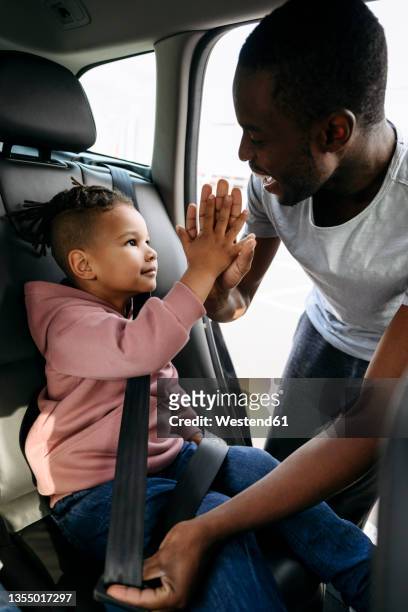 father giving high-five to son while fastening seat belt in car - black man high 5 stockfoto's en -beelden