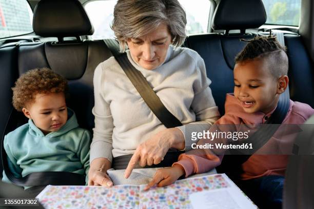 grandmother reading book with grandchildren in car - car young and old person stock pictures, royalty-free photos & images