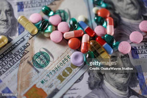 pills and capsules over one-hundred-dollar bills - prescription drug costs stock pictures, royalty-free photos & images