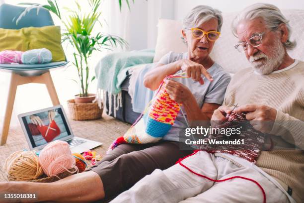 woman teaching man to knit wool with needle at home - masche stock-fotos und bilder
