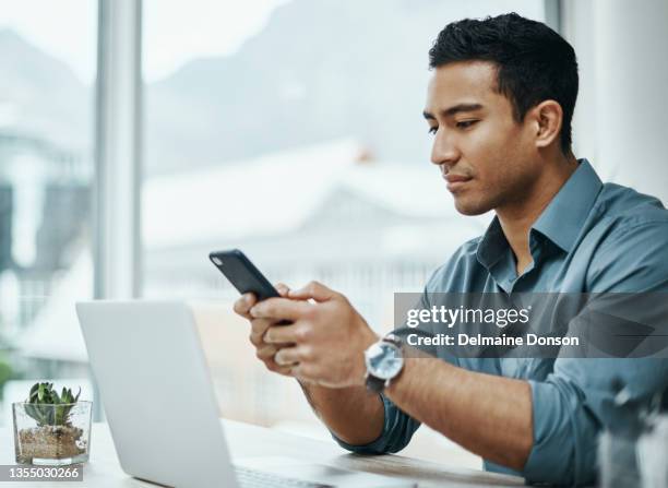 shot of a young businessman using a smartphone and laptop in a modern office - man texting stockfoto's en -beelden