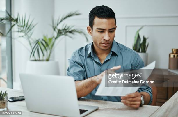 foto de un joven empresario usando una computadora portátil y revisando el papeleo en una oficina moderna - audit fotografías e imágenes de stock