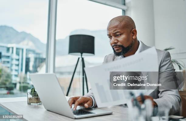 shot of a mature businessman using a laptop and going over paperwork in a modern office - auditoria imagens e fotografias de stock