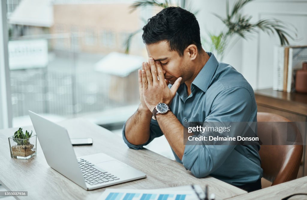 Shot of a young businessman looking stressed while working in a modern office