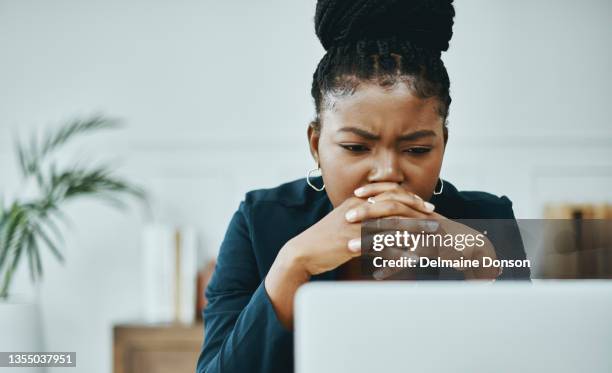 shot of a young businesswoman frowning while using a laptop in a modern office - black woman laptop stockfoto's en -beelden