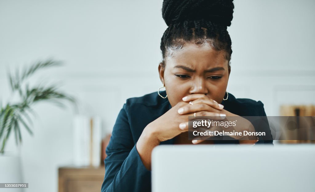 Shot of a young businesswoman frowning while using a laptop in a modern office