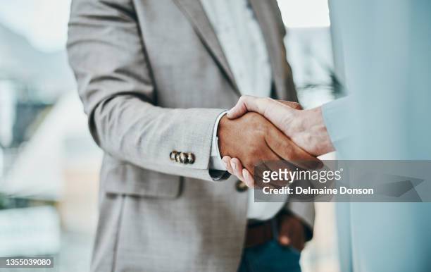 shot of a businessman and businesswoman shaking hands in a modern office - business agreement stock pictures, royalty-free photos & images