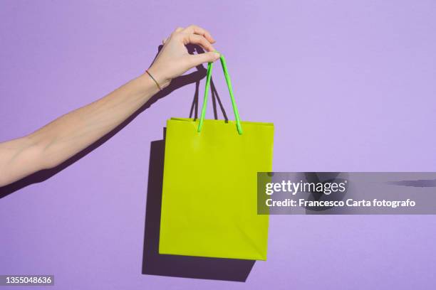 woman's hand carrying colorful shopping bag - geschenktüte einwickelpapier stock-fotos und bilder