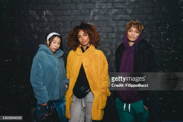 retrato de tres amigos de moda juntos contra una pared de ladrillos negros - black teenage models fotografías e imágenes de stock