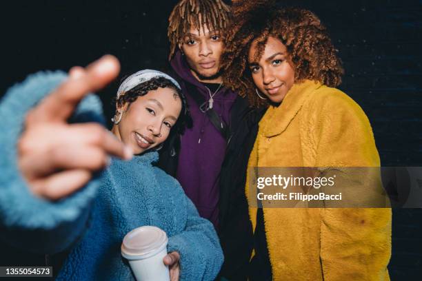 portrait of three friends against a black bricks wall, making gestures in front of the camera - rap group stockfoto's en -beelden