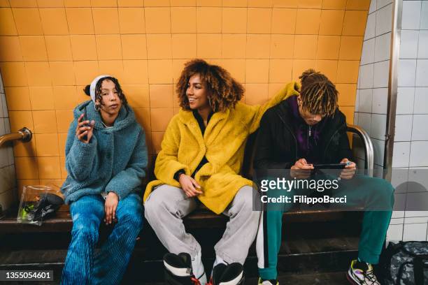 drei freunde warten in einer u-bahn-station auf den zug - londoner u bahn stock-fotos und bilder