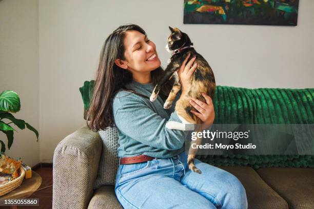 cropped shot of an attractive young woman petting her cat while chilling in the living room at home - huisdiereigenaar stockfoto's en -beelden