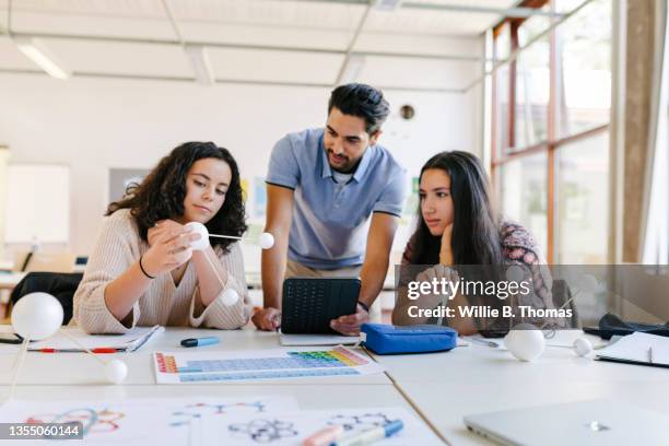 high school science teacher with tablet explaining model to two students - teacher desk fotografías e imágenes de stock