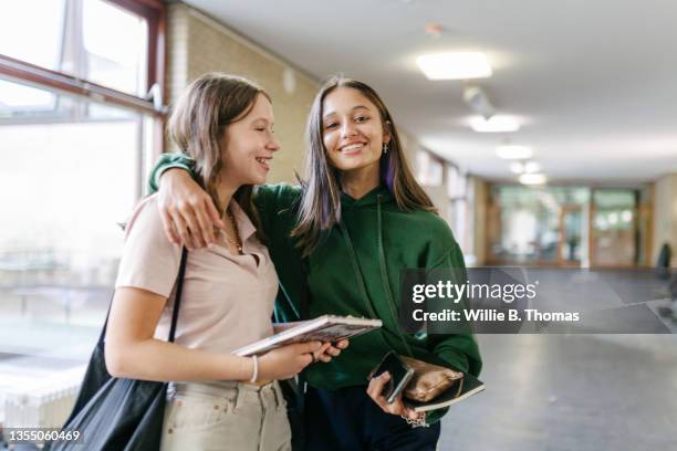 two students hugging each other on their way to class - alleen tienermeisjes stockfoto's en -beelden
