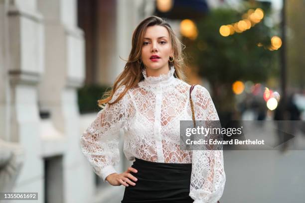 Olesya Senchenko wears a white lace turtleneck shirt / blouse, a burgundy shiny leather crocodile print pattern Sunset shoulder bag from Yves Saint...