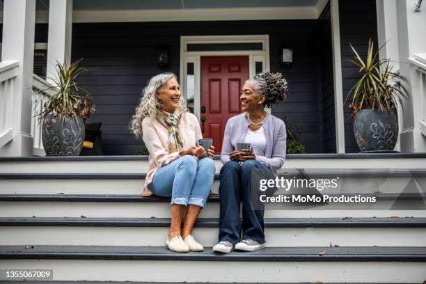 senior women having coffee in front of suburban home - woman on porch steps stock pictures, royalty-free photos & images