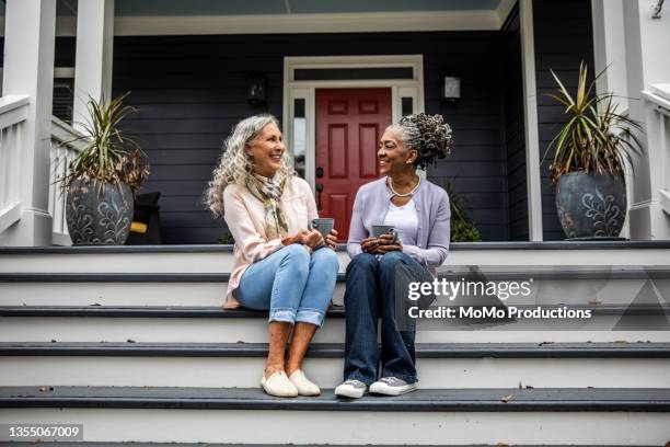 senior women having coffee in front of suburban home - female with friend in coffee stock pictures, royalty-free photos & images