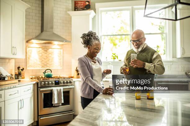 senior couple taking vitamin supplements in kitchen of suburban home - vitaminas fotografías e imágenes de stock