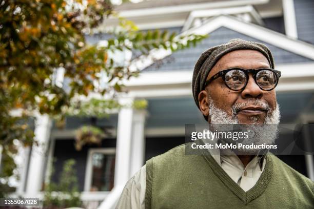 portrait of senior man in front of suburban home - black glasses stock-fotos und bilder