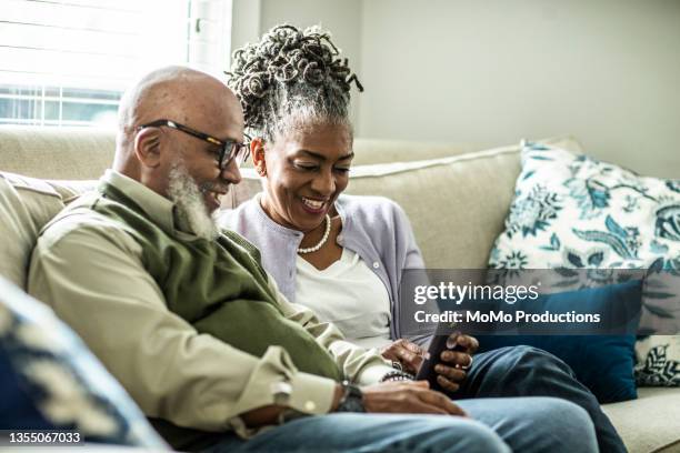 senior couple looking at smartphone in living room of suburban home - couple smartphone stock pictures, royalty-free photos & images