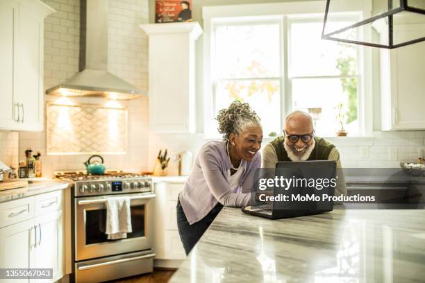 senior couple using laptop in kitchen of suburban home - share my wife fotos stock-fotos und bilder
