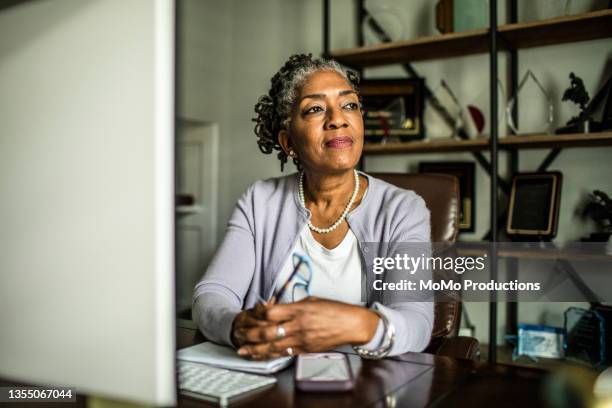 portrait of senior woman at desktop computer in home office - focus noir photos et images de collection