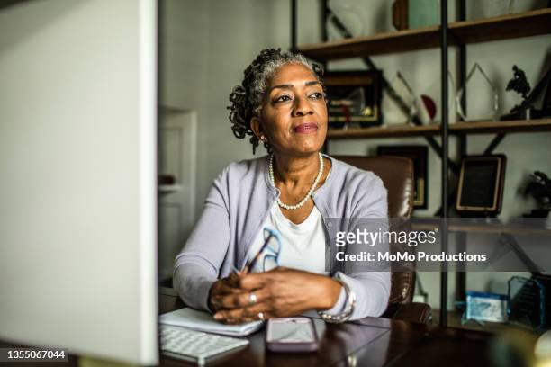 portrait of senior woman at desktop computer in home office - reflective stockfoto's en -beelden