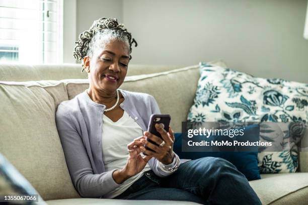 senior woman using smartphone in living room of suburban home - senior adult on phone stock pictures, royalty-free photos & images