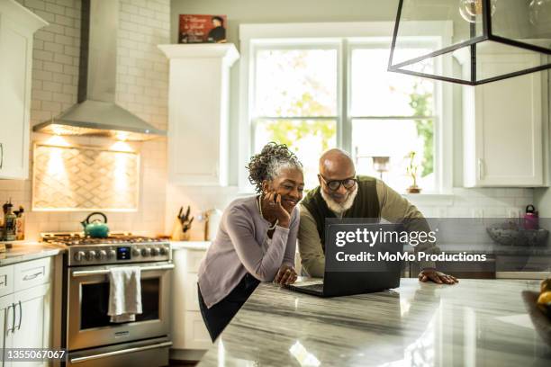 senior couple using laptop in kitchen of suburban home - retires ストックフォトと画像