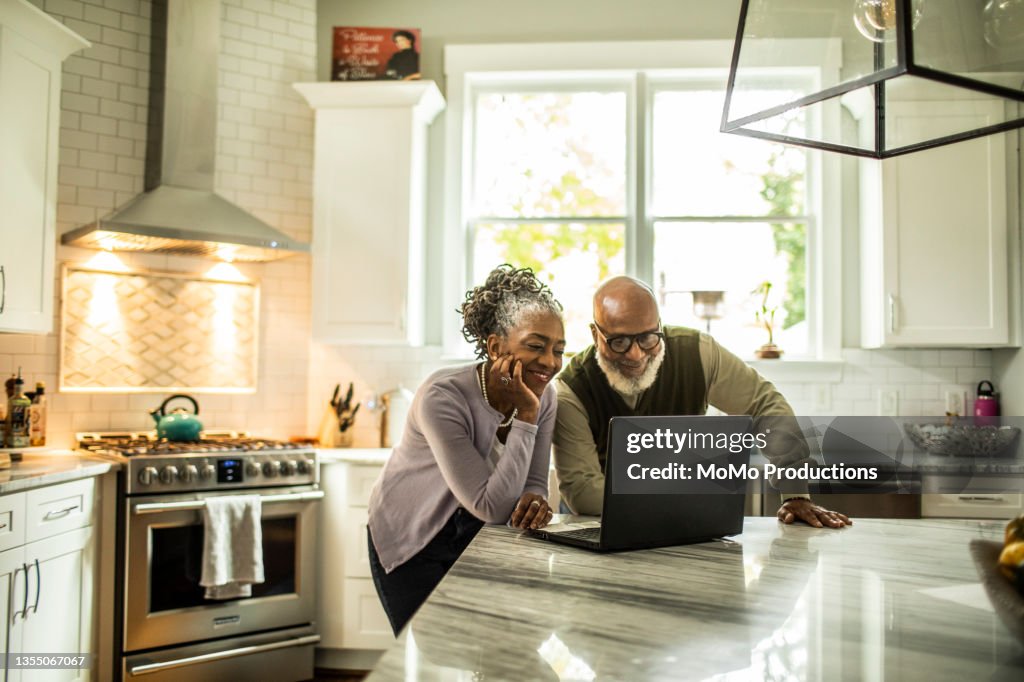 Senior couple using laptop in kitchen of suburban home