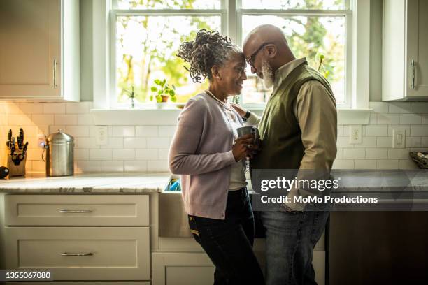 senior couple embracing in kitchen of suburban home - falling in love stock pictures, royalty-free photos & images