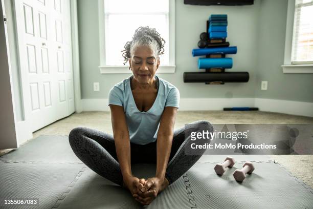 senior woman exercising in home gym - yoga pose stockfoto's en -beelden