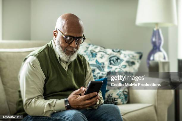 senior man using smartphone in living room of suburban home - call us photos et images de collection