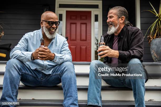 senior men having beers and talking on front porch - 60 69 years stock pictures, royalty-free photos & images