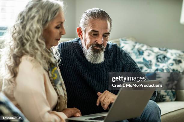 senior couple using laptop in living room of suburban home - share my wife fotos stock-fotos und bilder