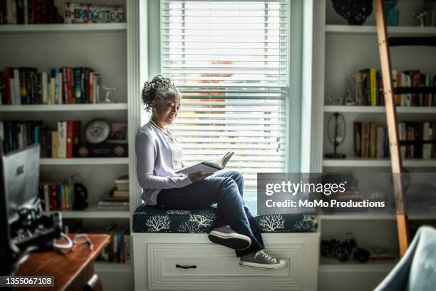 senior woman reading in home library - bookshelf foto e immagini stock