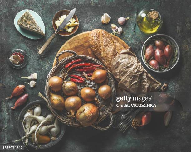 tasty french onion soup ingredients: various onions, garlic, cheese, olive oil, baguette and butter on rustic dark kitchen table - onion soup stock pictures, royalty-free photos & images