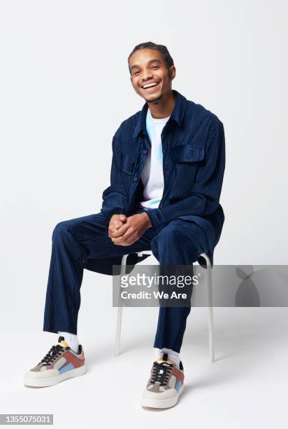 portrait of young man sitting on stool in studio - ledig kontorsklädsel bildbanksfoton och bilder