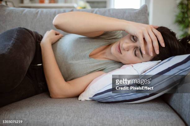 despair young female lying on the couch suffering from headache - hoofdpijn vrouw stockfoto's en -beelden
