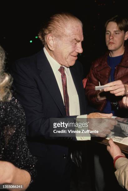 American actor Lionel Stander , wearing a dark blue blazer with a white shirt and deep red tie, signing autographs for fans, circa 1990.