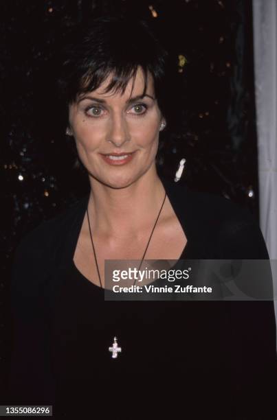 Irish singer-songwriter and musician Enya, wearing a long black dress with a scoop neckline, with a crucifix pendant hanging around her neck, attends...