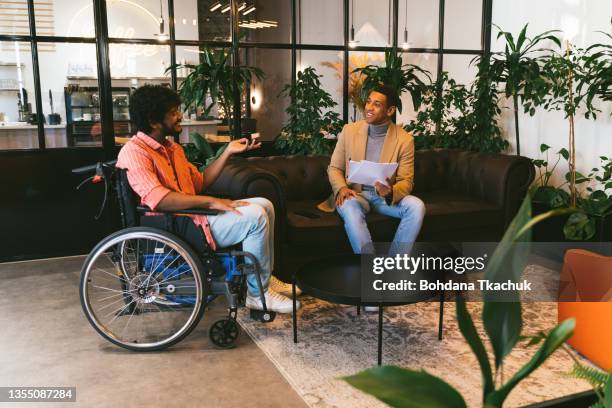 gemischtrassige executive associates treffen im büroempfangsraum und austausch von ideen in der sitzecke eines modernen büro-coworking-platzes. behinderter indischer geschäftsmann im rollstuhl - rehabilitation meeting stock-fotos und bilder