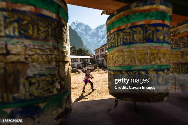 a woman is hiking past prayer wheels at tengboche monastery, nepal. - népal photos et images de collection