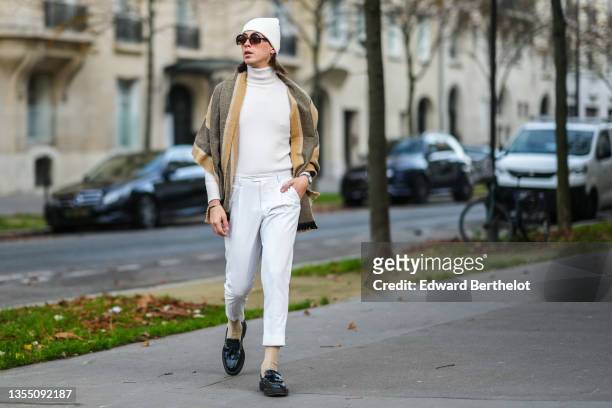Marco Capaccioli wears sunglasses from Miu Miu, a white ribbed wool beanie, a white cashmere turtleneck pullover from Falconeri, a beige / khaki /...