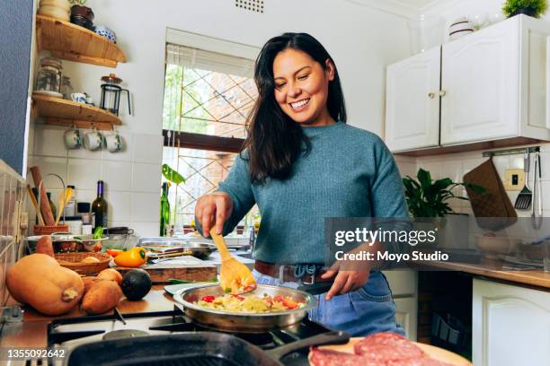 shot of a young woman stirring vegetables on the stove - stirring stock pictures, royalty-free photos & images